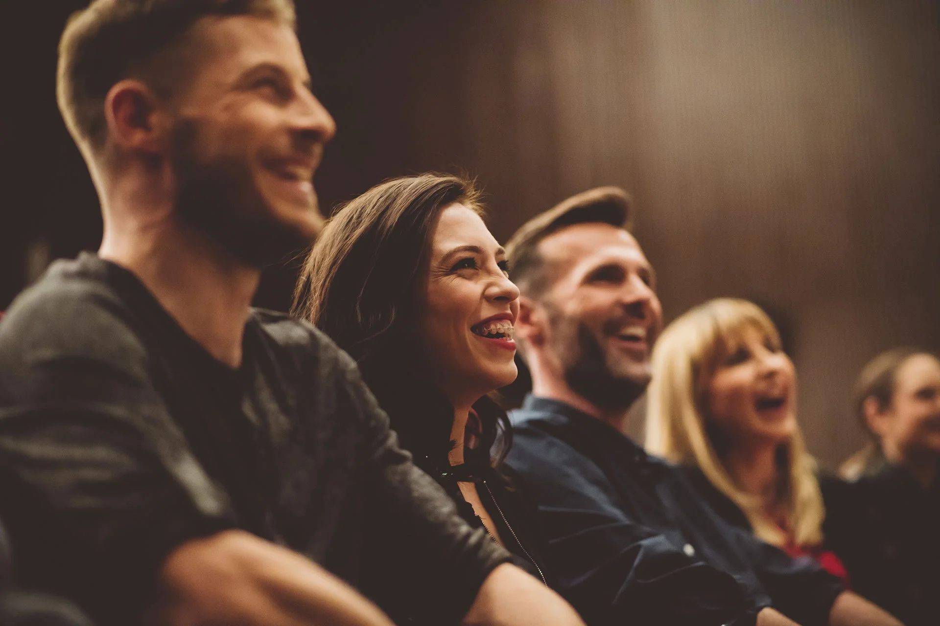 Group of five people sitting in an audience, smiling and enjoying a performance or presentation.