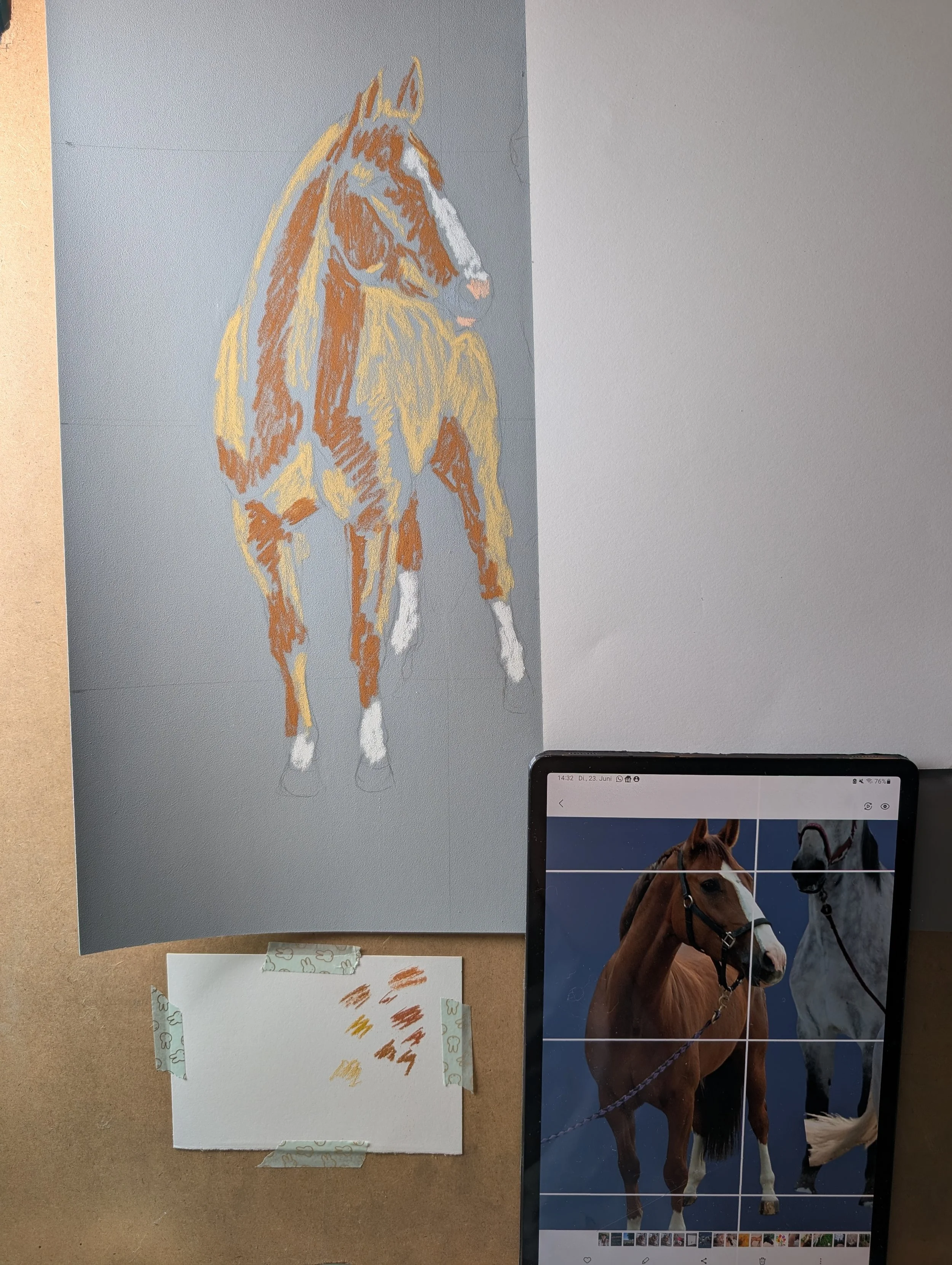 Eine digitale Bildbearbeitungssoftware zeigt ein Bild eines braunen Pferdes auf dem Bildschirm, während auf einer Tafel daneben eine Pferdezeichnung in Pastellfarben und Farbtöne zum Vergleich, sowie Farbbeispiele auf Notizzetteln zu sehen sind.