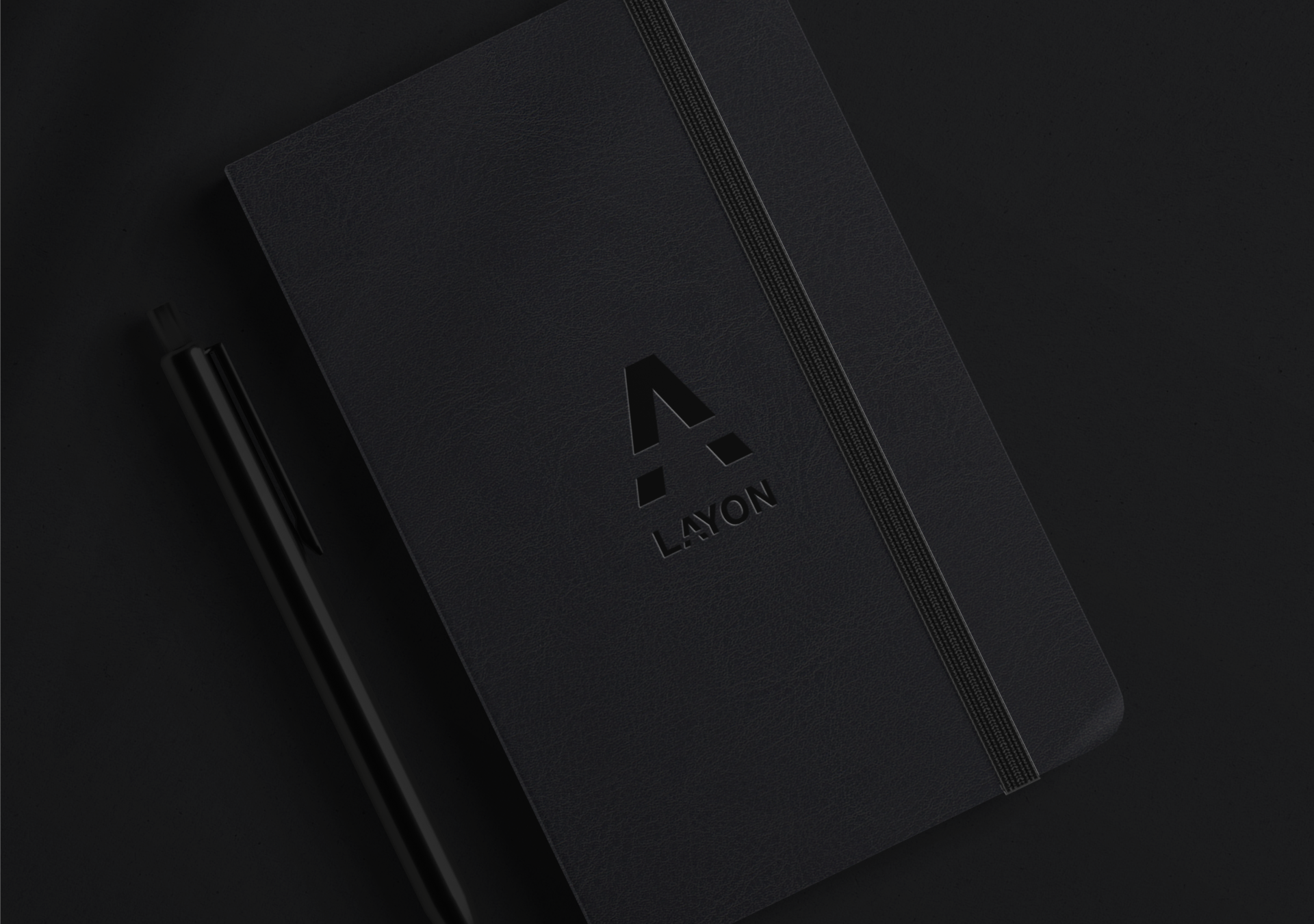 Cuaderno negro con logotipo de Layon y pluma negra sobre fondo negro.