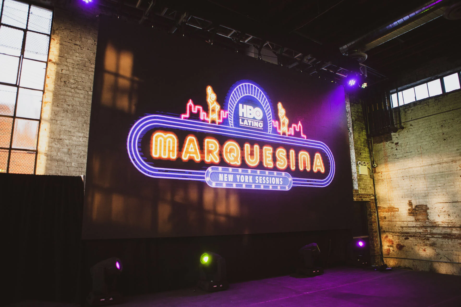 Pantalla de neon que dice 'Marquesina' en un fondo oscuro, con una construcción de ladrillos expuesta y luces de escenario.
