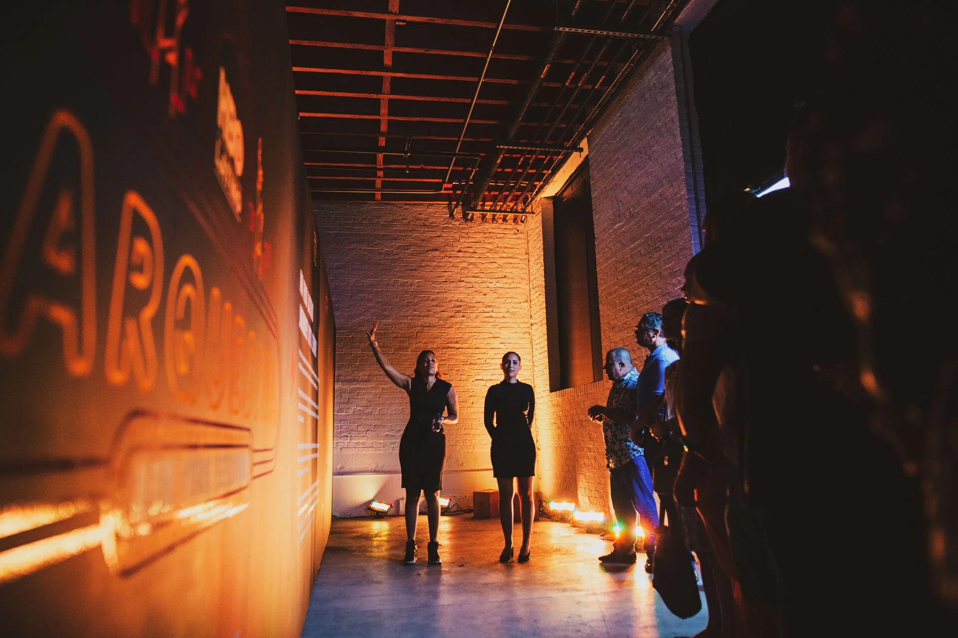 Grupo de personas en una presentación o evento en un espacio con paredes de ladrillo y iluminación de colores cálidos.