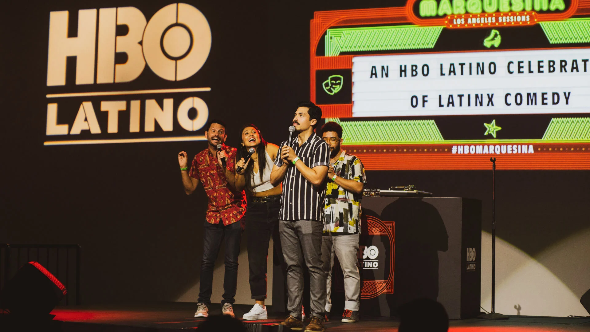 Grupo de comediantes en un escenario durante un evento de comedia latina organizado por HBO Latino, con un fondo que muestra el logo de HBO Latino y un letrero que dice 'Marquesina Los Angeles Sessions' y 'Un homenaje latino a la comedia de latinoame