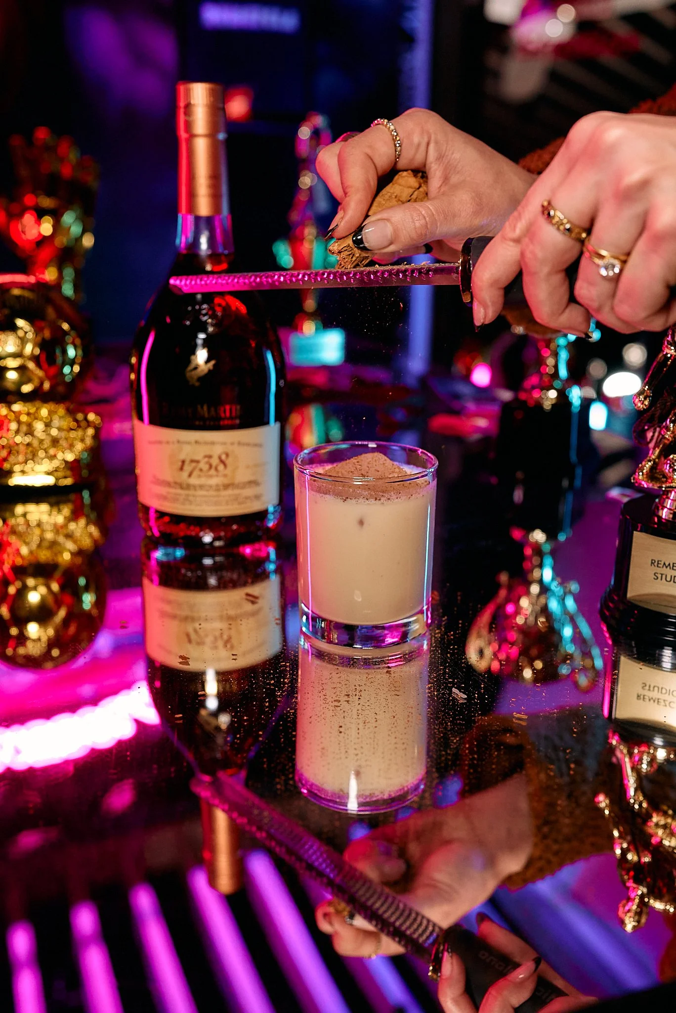 Persona decorando la copa de un cóctel en un bar con luces de neón y decoraciones festivas.