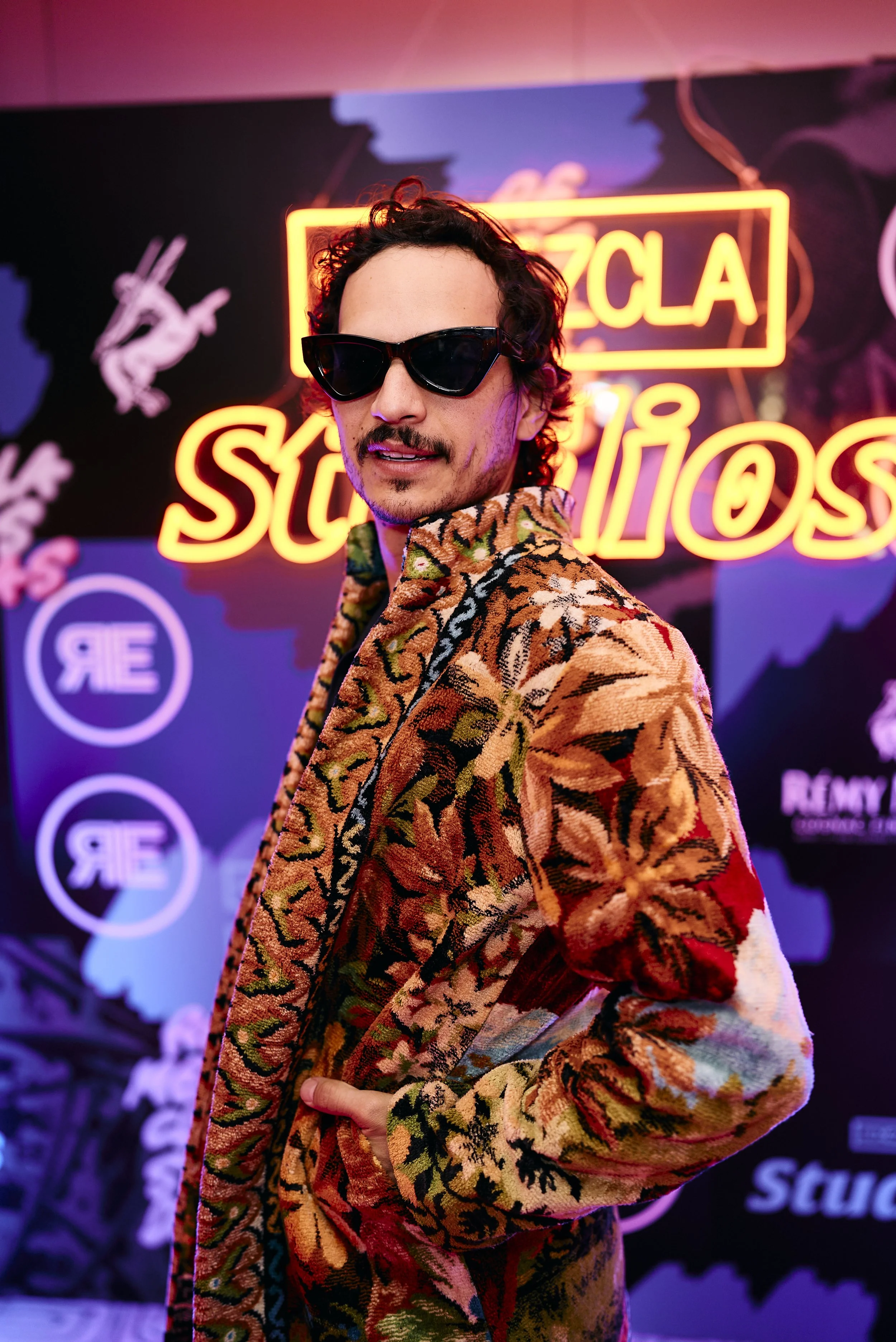 Hombre con gafas de sol y chaqueta con estampado floral en un evento con iluminación de neón