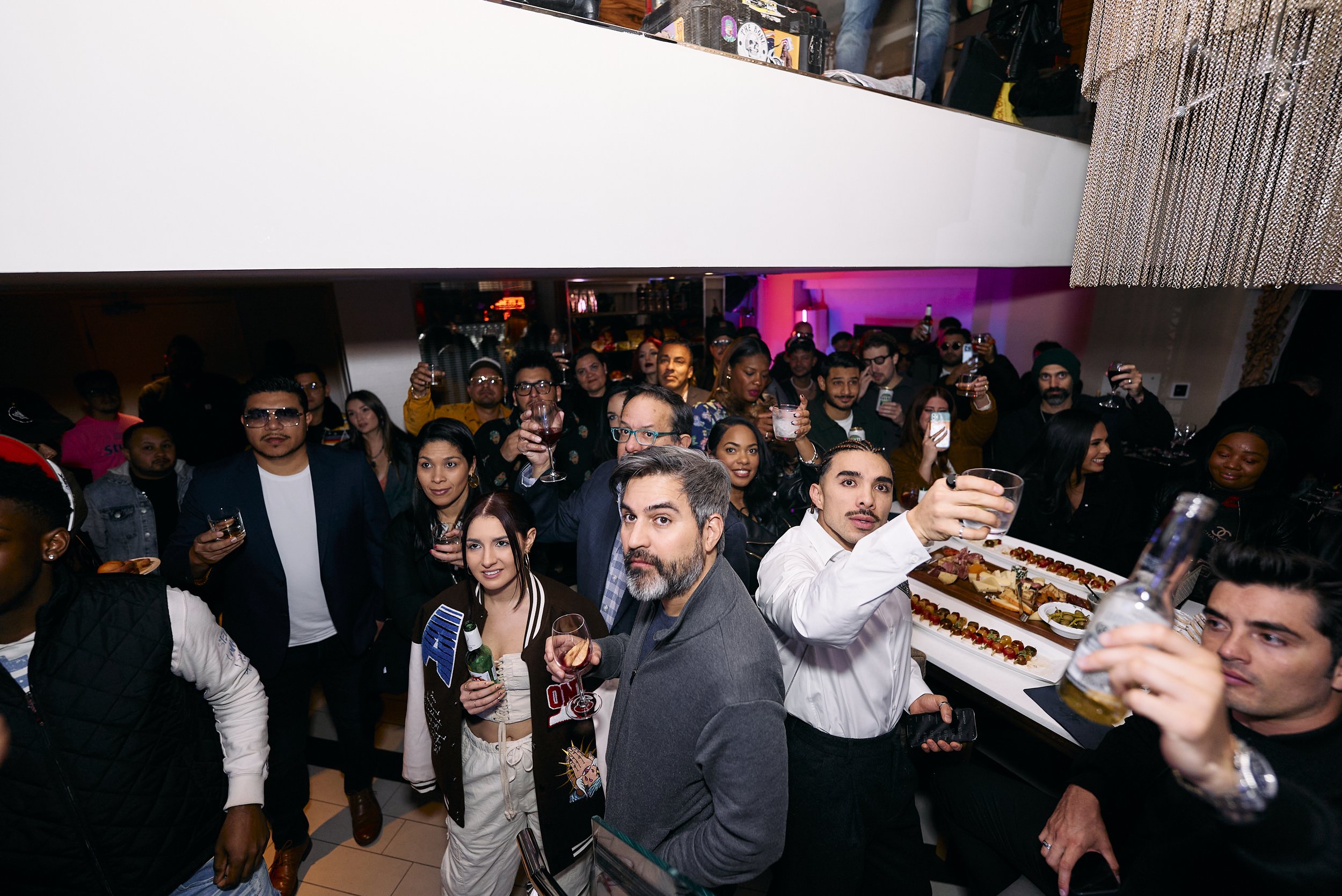 Grupo de personas en una fiesta, algunos sosteniendo bebidas, con un ambiente festivo y decoraciones coloridas.