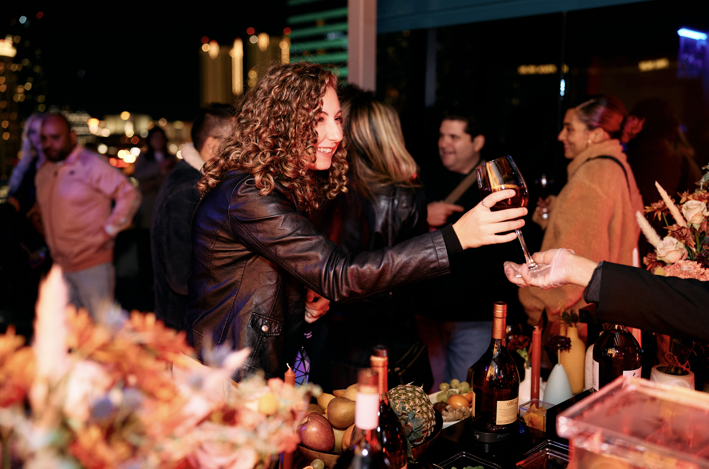Mujer sonriendo entregando una copa de vino a otra persona en un evento social nocturno.