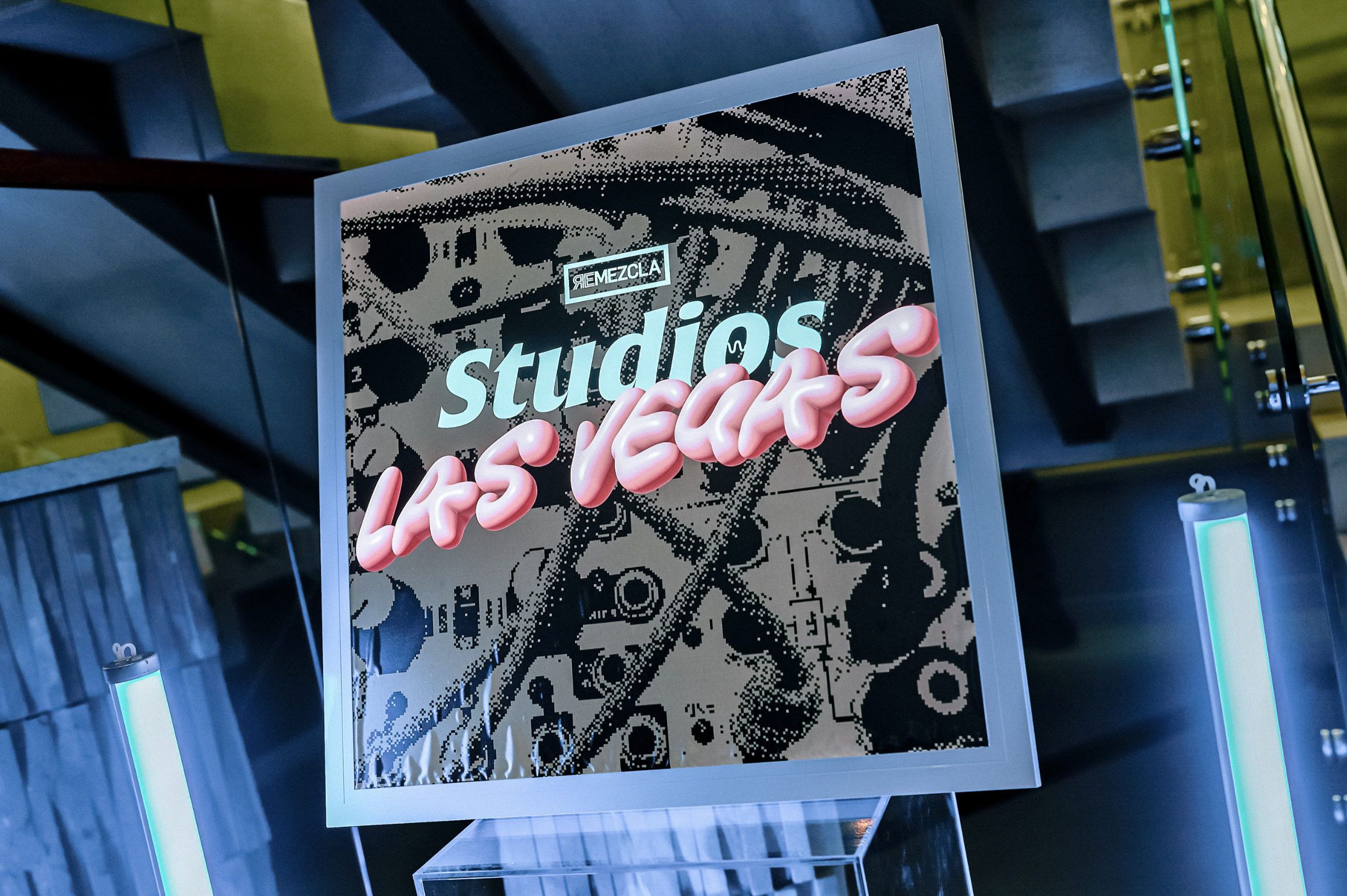 Cartel de neon que dice 'Remezcla studios Las Vegas' en un fondo de equipo de DJ en colores oscuros y acento en azul y rosa.