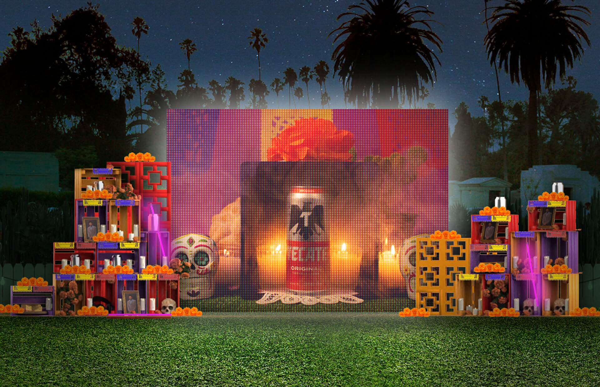 Altar del Día de los Muertos decorado con calaveras, flores naranjas, fotografías y velas, frente a una pantalla LED gigante en un parque, con árboles y un cielo estrellado al fondo.