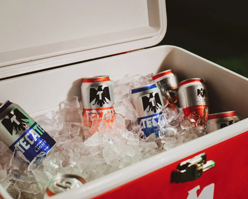 Recipiente rojo con hielera llena de hielo y varias latas de cerveza en su interior.