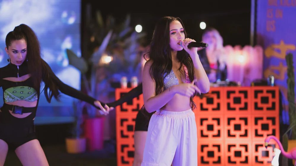 Joven mujer cantando con micrófono en mano durante un espectáculo con luces y decoraciones coloridas.