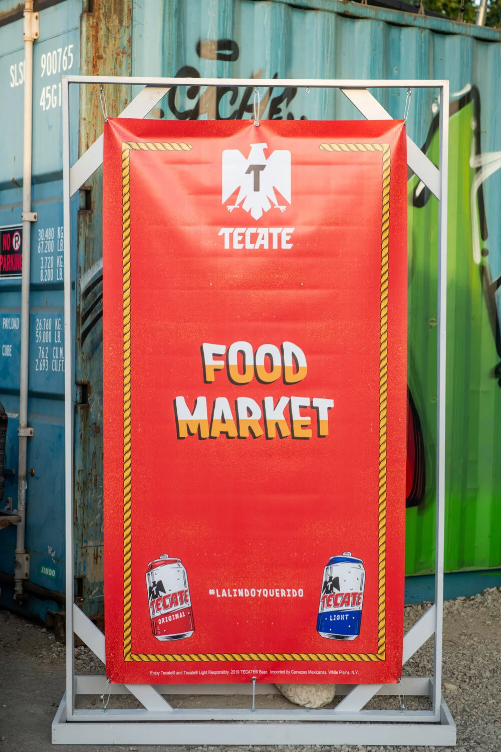Cartel de mercado de comida con logotipo de Tecate y dos latas de cerveza, una roja y otra azul.