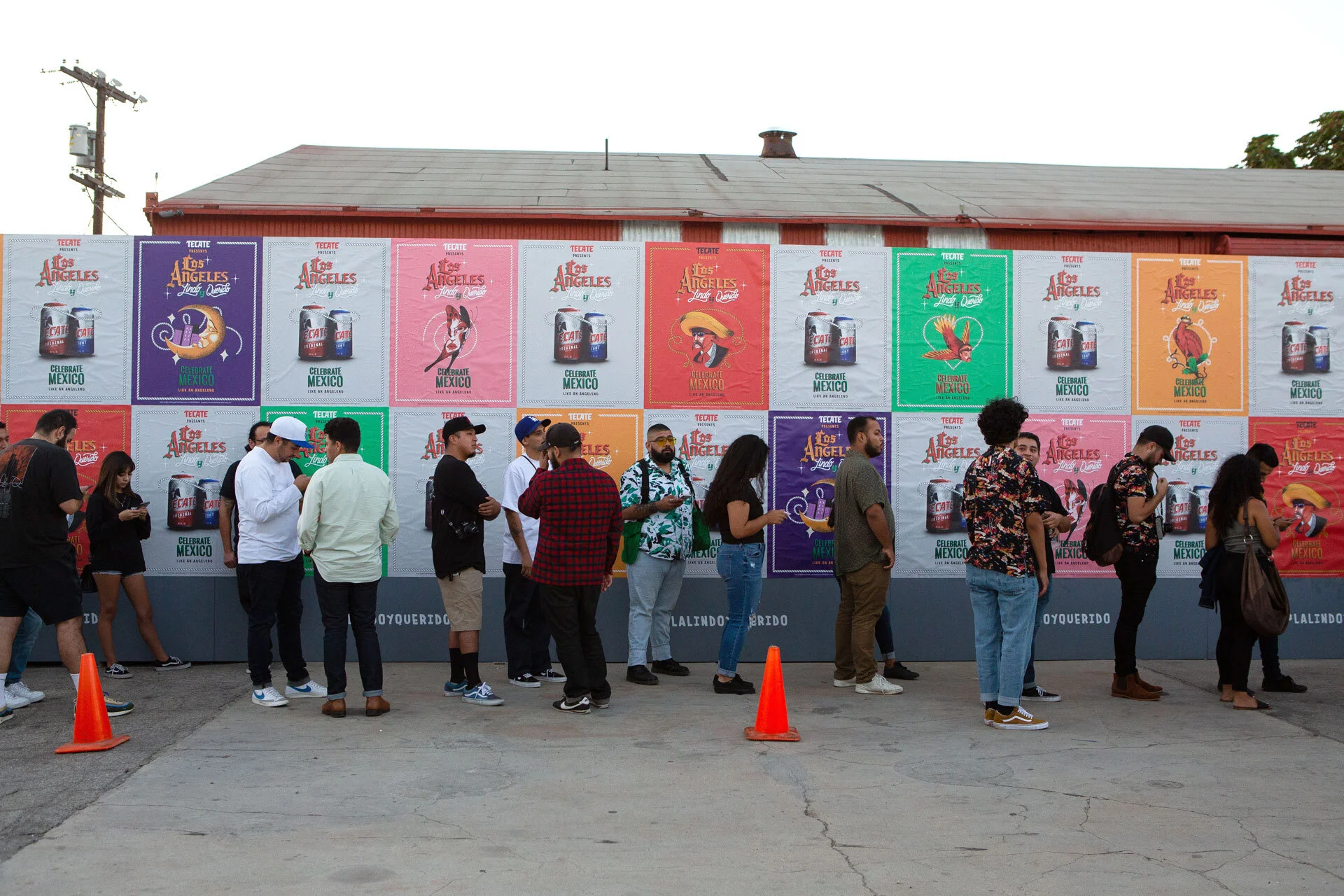 Personas haciendo fila para un evento de Los Ángeles y Tecate, con carteles coloridos en la pared que celebran México, mostrando una bebida y temas culturales.