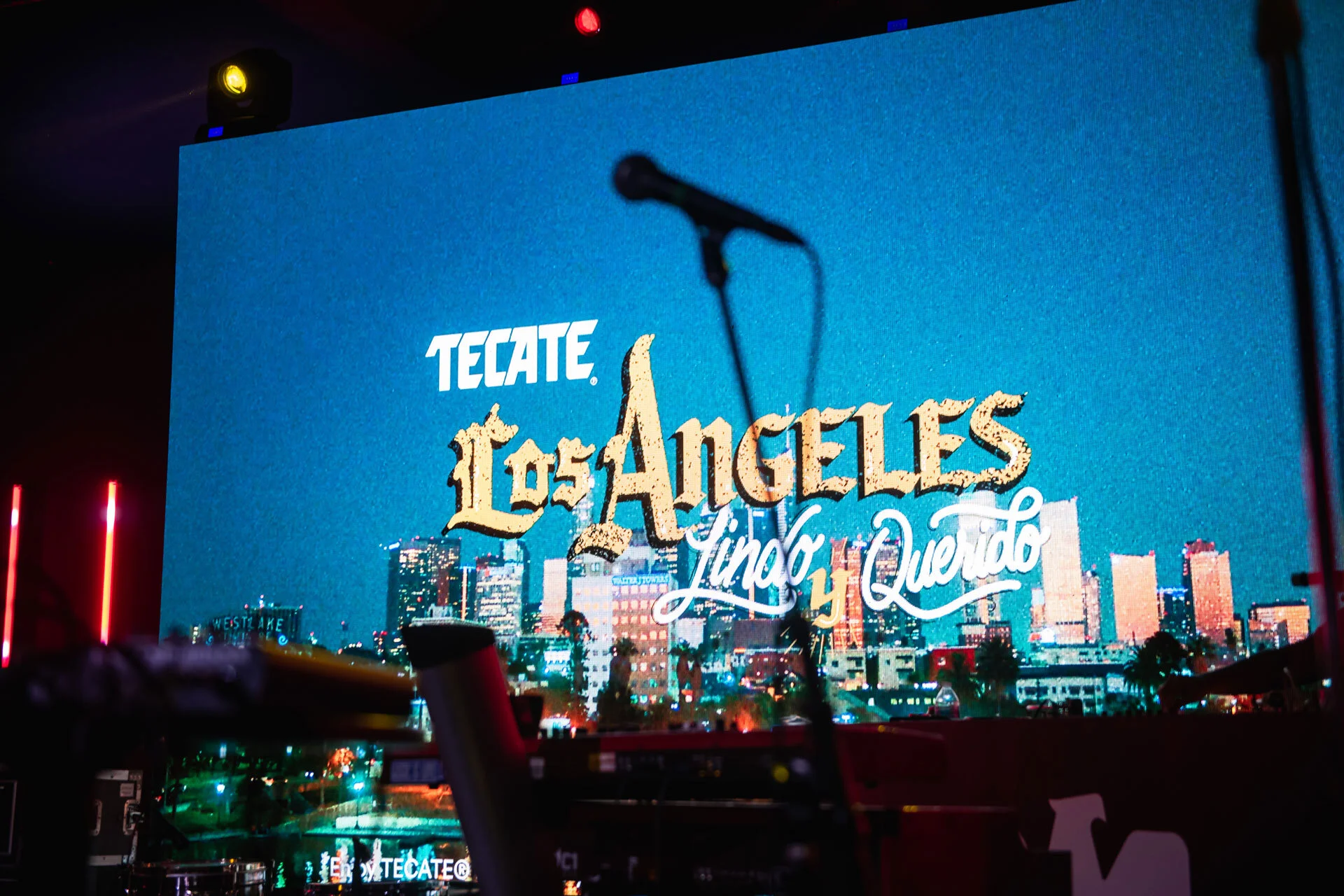 Pantalla gigante en un evento con el logo de Tecate y una imagen de Los Ángeles con luces de ciudad de noche.