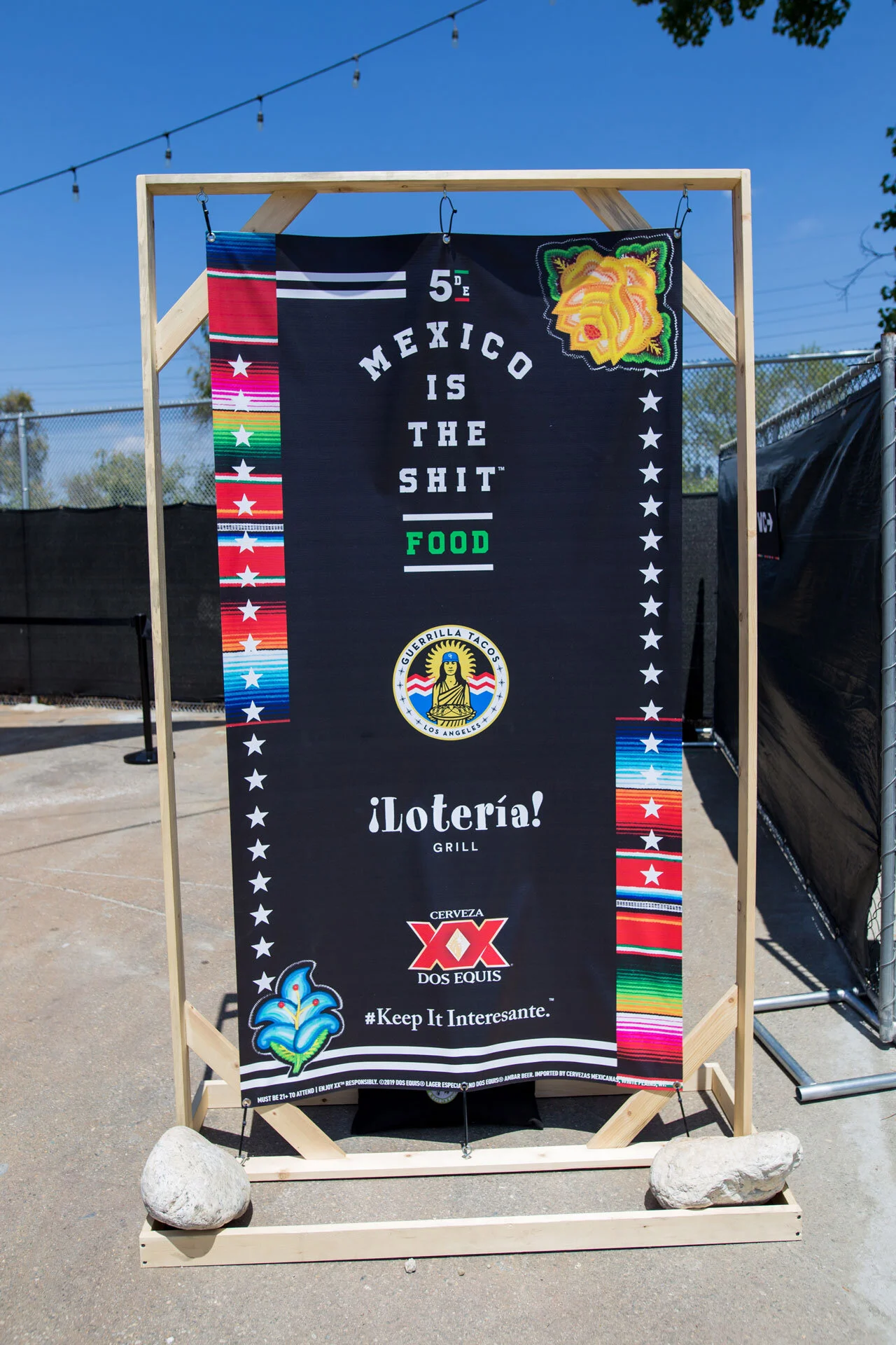 Cartel con texto en inglés y otros elementos decorativos en un marco de madera en un espacio al aire libre, con cielo azul y árboles en el fondo.