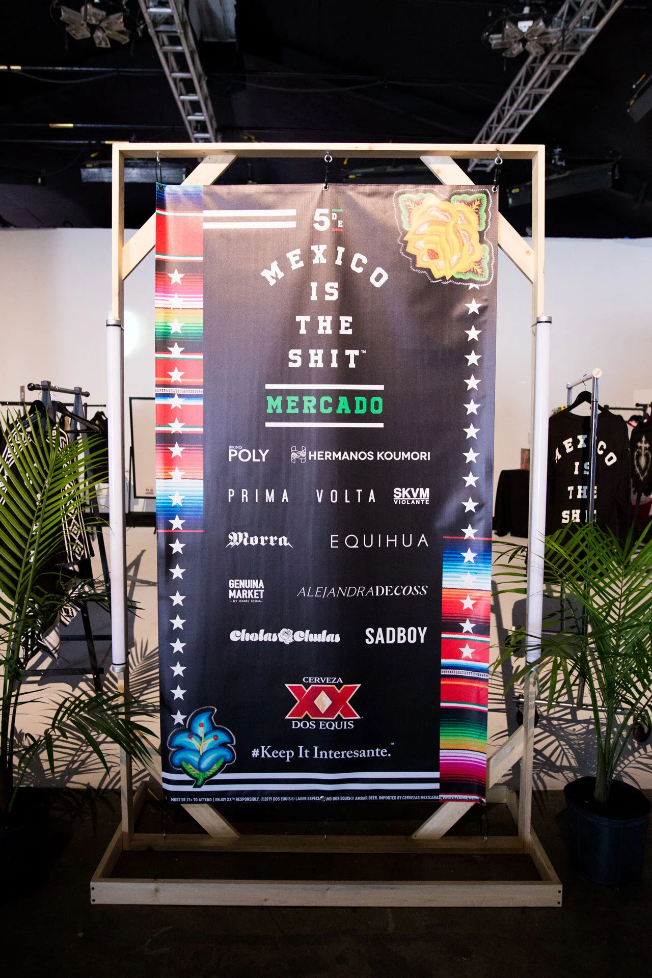 Cartel promocional con fondo negro y borde de colores con imágenes de la bandera mexicana, con texto en inglés y español que dice 'México es la mierda' y nombres de marcas y artistas, acompañado de logotipo de cerveza Dos Equis y un hashtag '#KeepItI