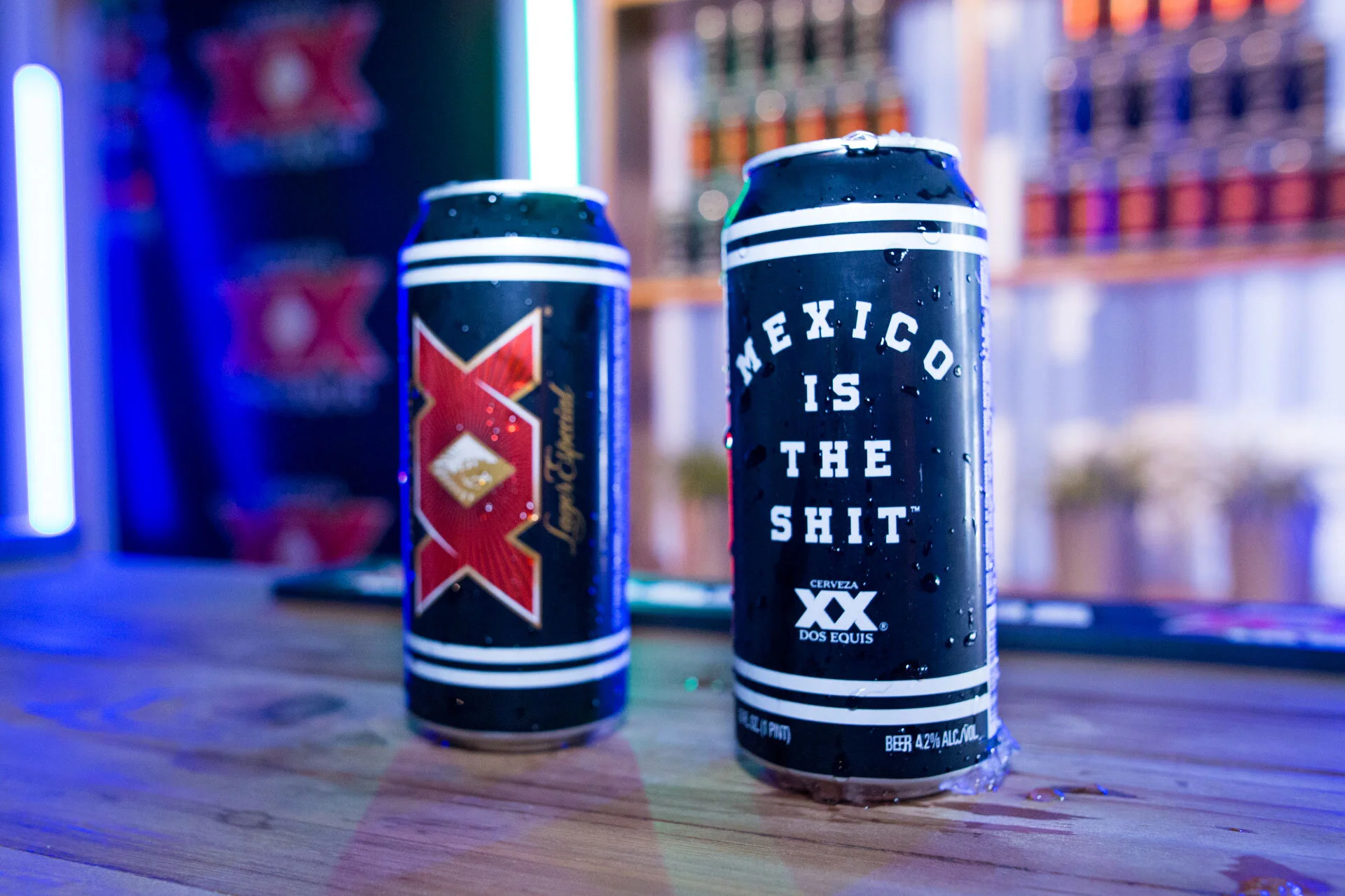 Latas de cerveza en un bar, una con un mensaje que dice "Mexico is the shit" y otra con un diseño de logo de cerveza.