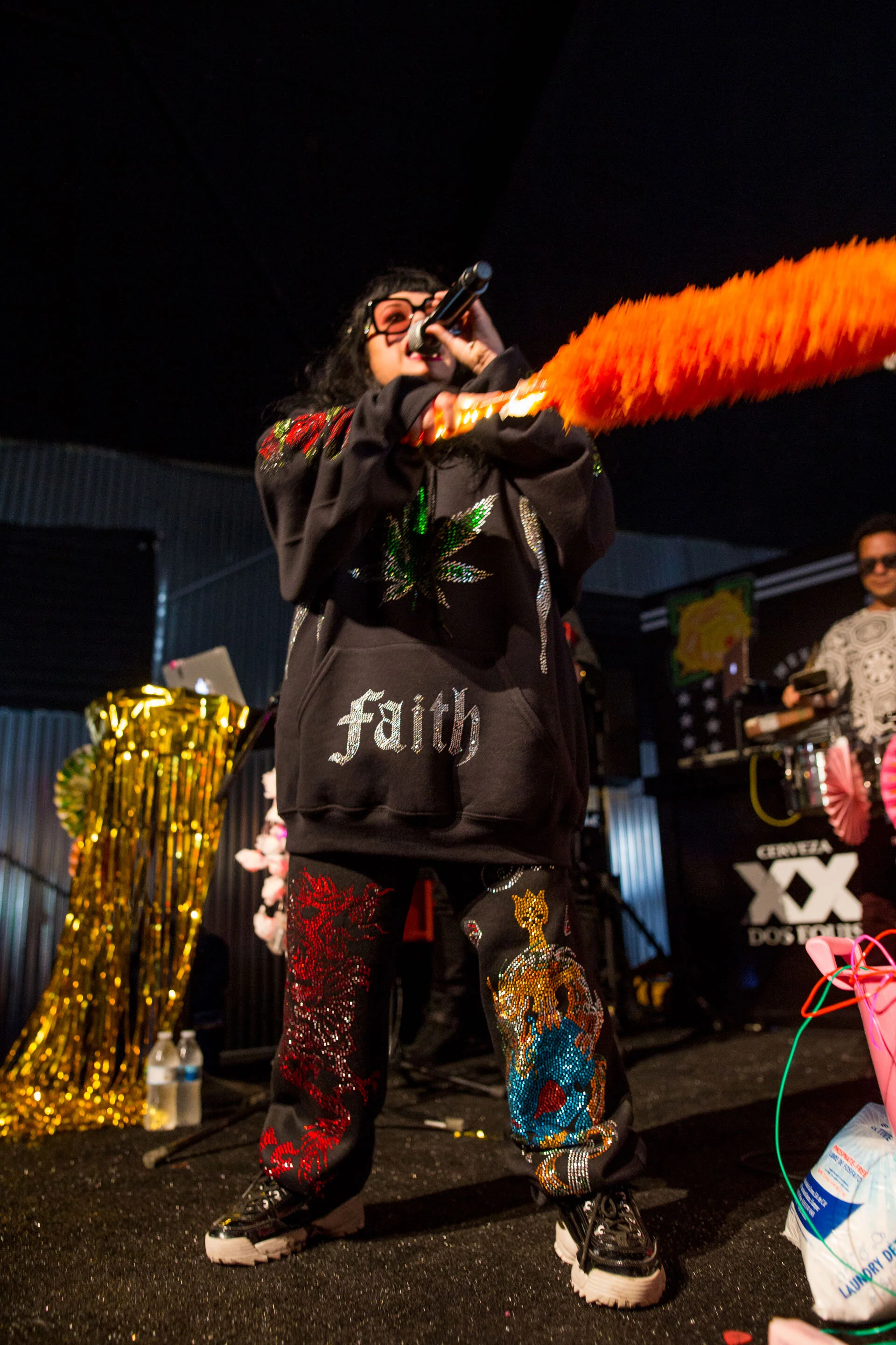 Persona en escenario con micrófono y vestimenta colorida con diseños llamativos, en ambiente de presentación o espectáculo.