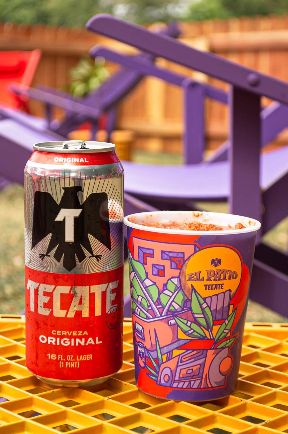 Lata de cerveza Tecate y un vaso con comida en un patio con sillas moradas.