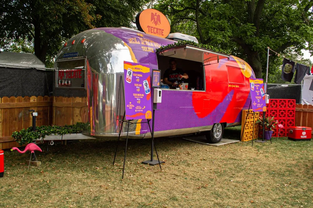 Food truck de tacos con decoración colorida y cartel de Menú, en un ambiente al aire libre con árboles y valla de madera.