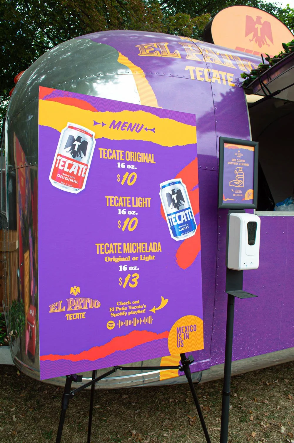 Menú de bebidas de un puesto móvil de Tecate en colores morado, amarillo y naranja. Lista de opciones con los precios: Tecate original y Tecate Light, ambos de 16 onzas por $10, y Tecate Michelada por $13. Incluye instrucciones para escanear un códig