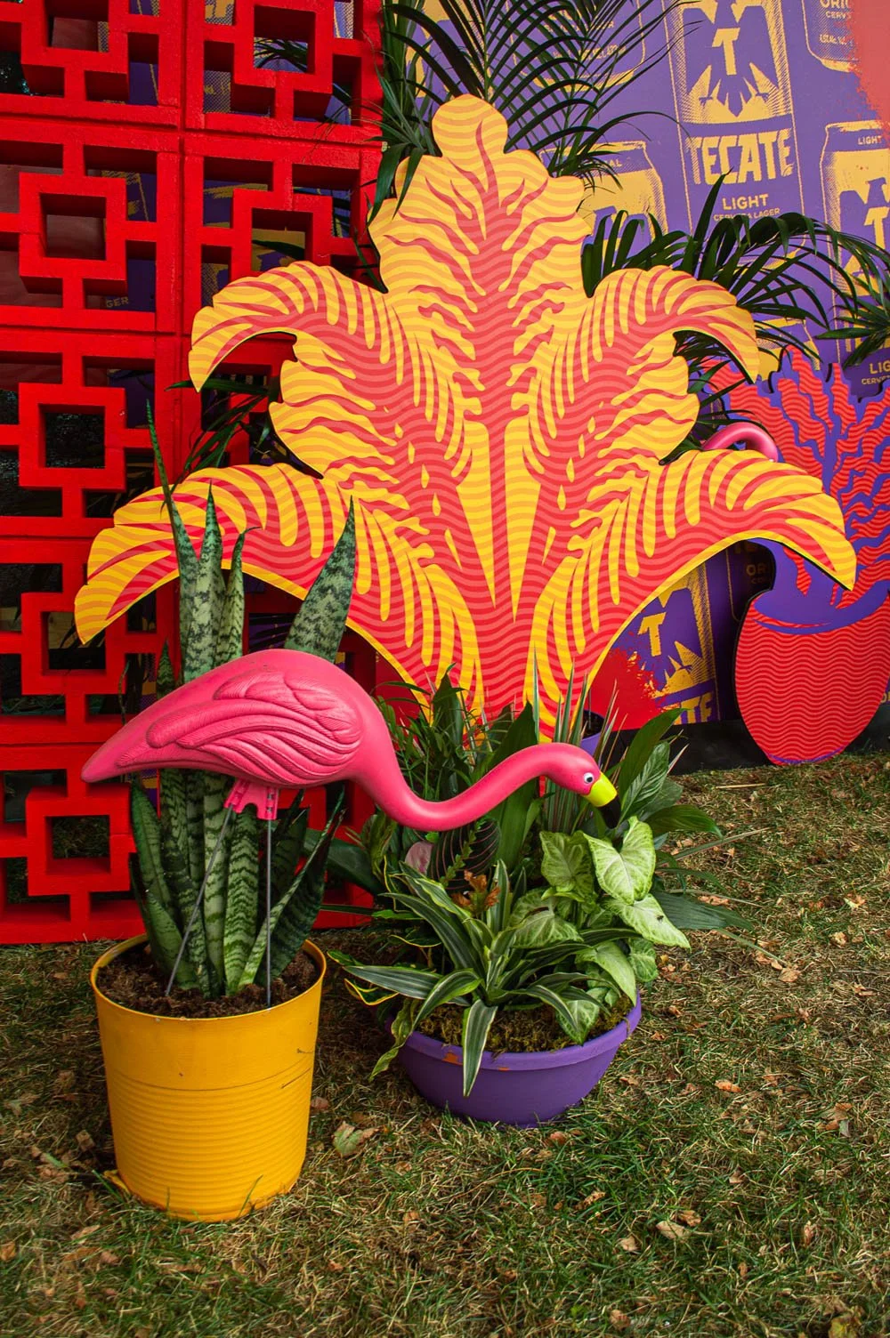 Plantas y decoraciones coloridas con un flamenco de plástico rosa y fondo con un mural vibrante que incluye hojas grandes y un patrón de colores brillantes.