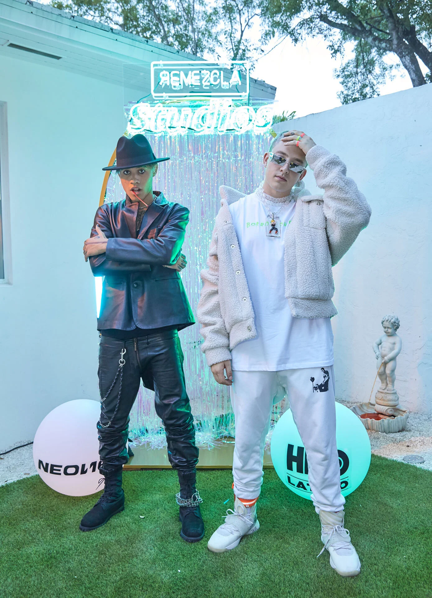 Dos personas con ropa moderna posan frente a una cortina de luces y decoraciones en un ambiente exterior