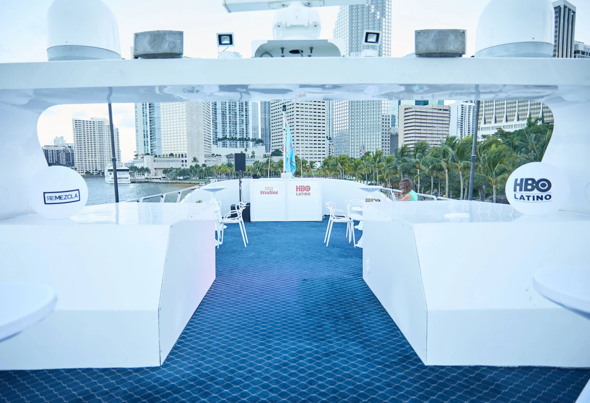 Espacio en una lancha con vista a un skyline de edificios altos en la ciudad, con árboles y agua a la orilla, decorado para un evento de HBO Latino.