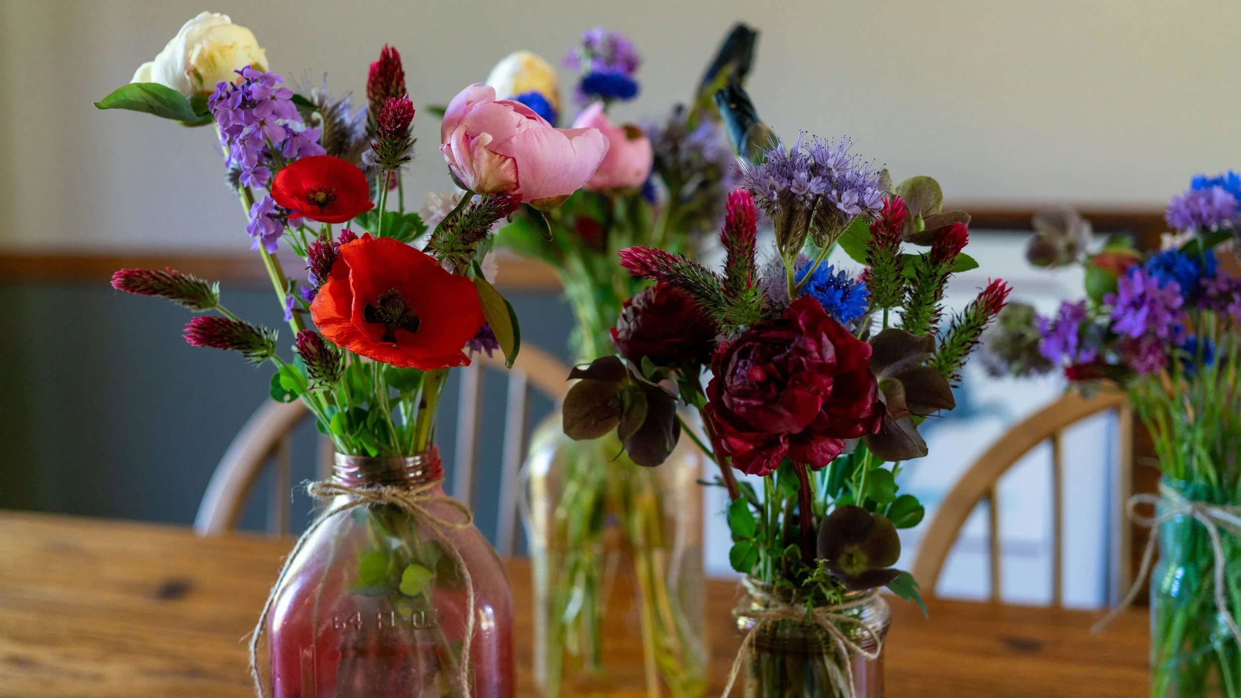 Vases with colorful flowers, including poppies and purple blooms, arranged on a wooden table.