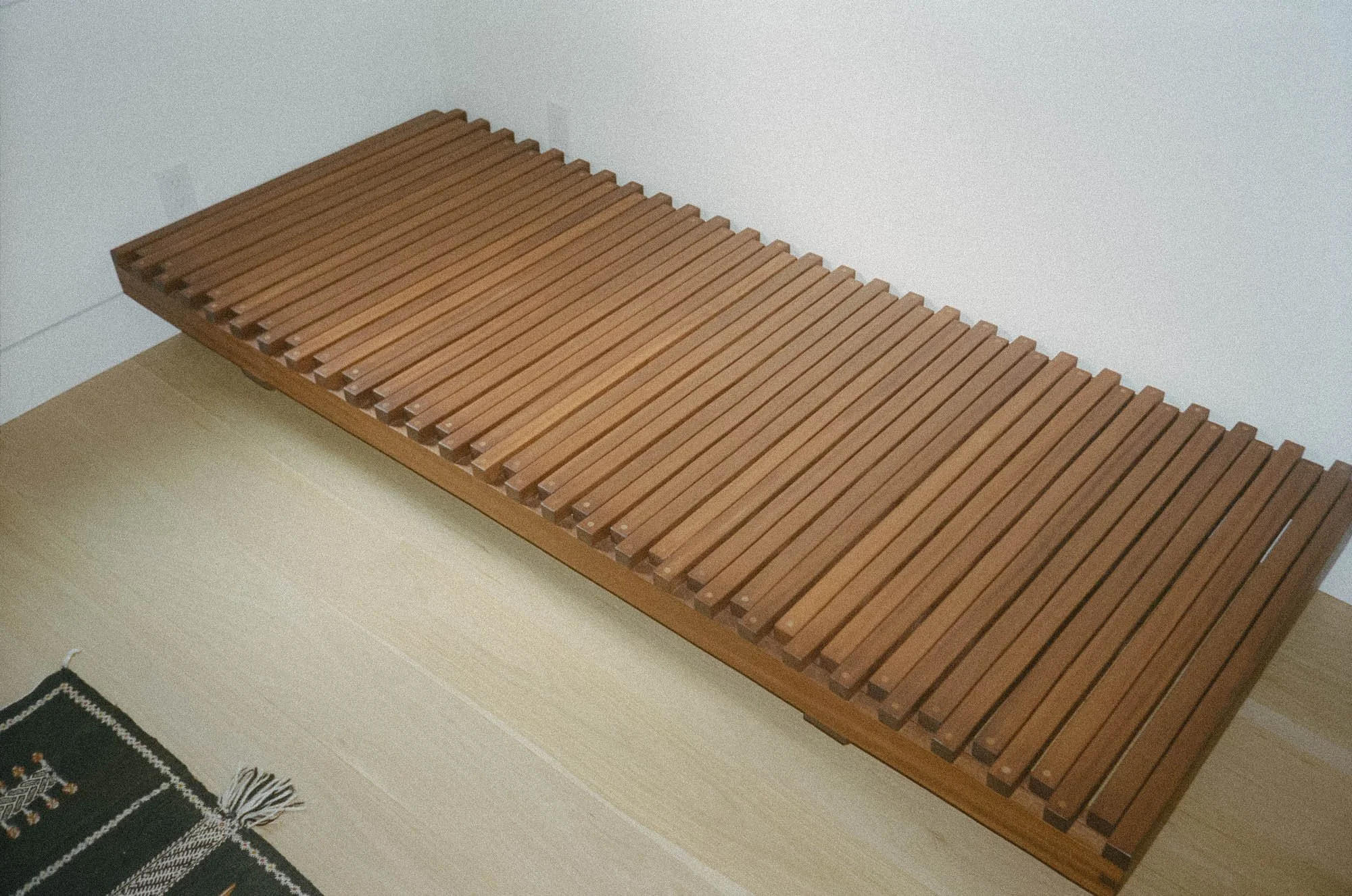 Wooden slatted daybed on a light-colored floor against a white wall.