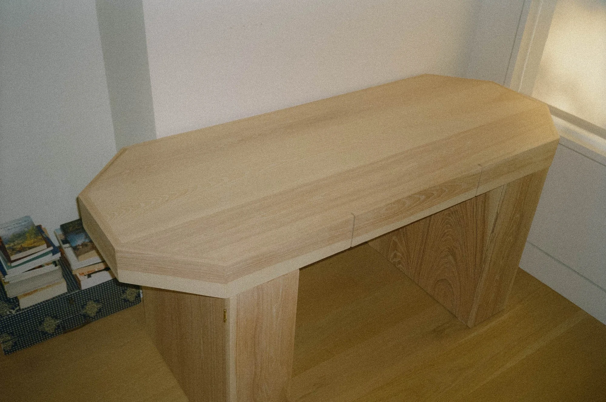 An octagonal shaped wooden desk in a room with light-colored walls and a wooden floor.