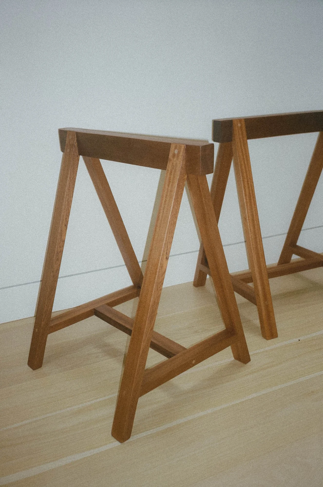 Two wooden sawhorses on a light-colored wooden floor against a plain white wall.