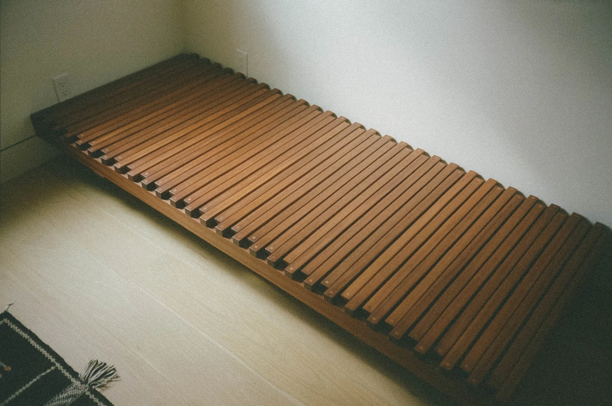 A wooden daybed made with slats positioned against a light-colored wall with electrical outlets.