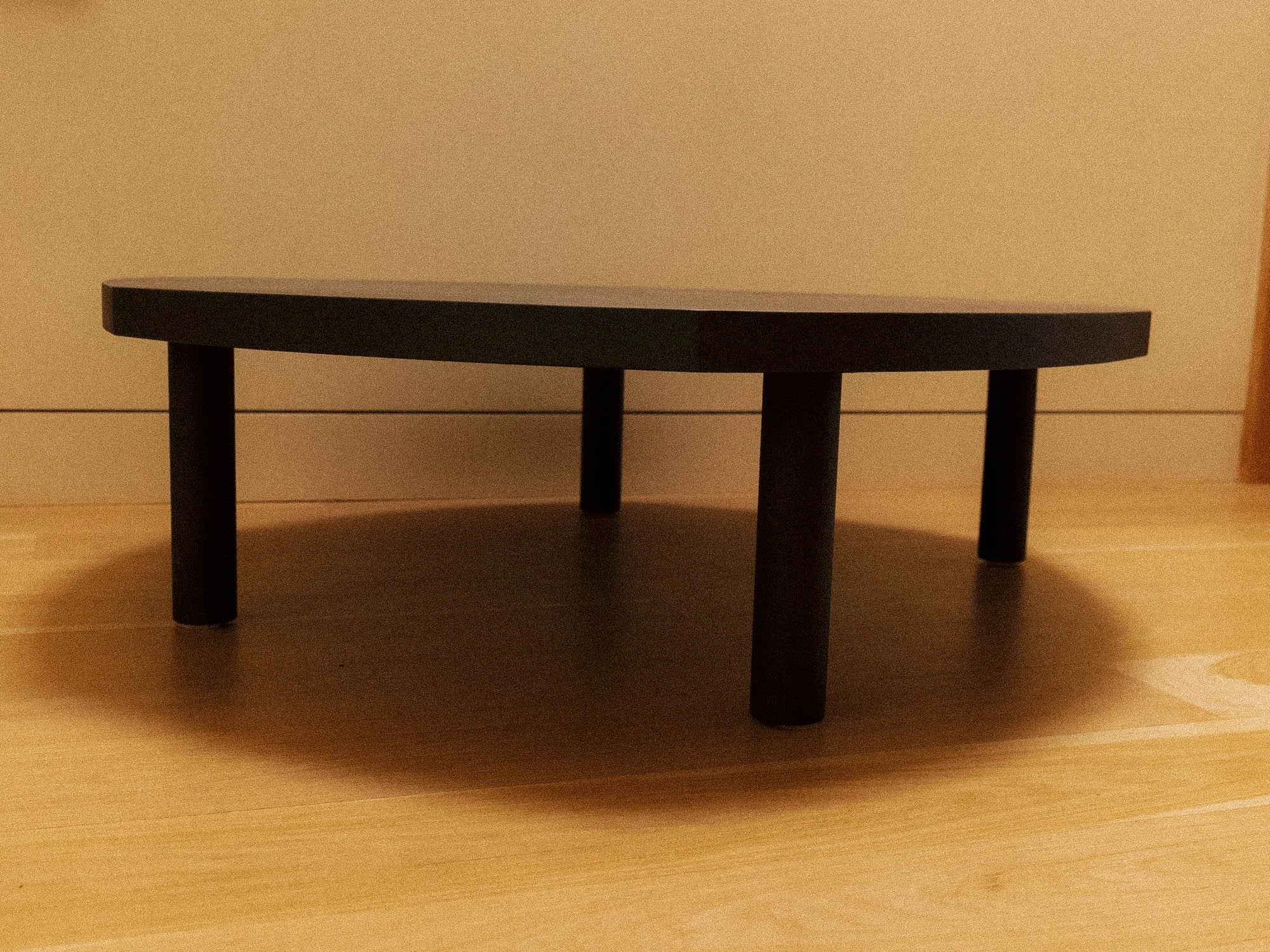 A coffee table with a black stained edge with four legs on a wood floor against a plain wall.