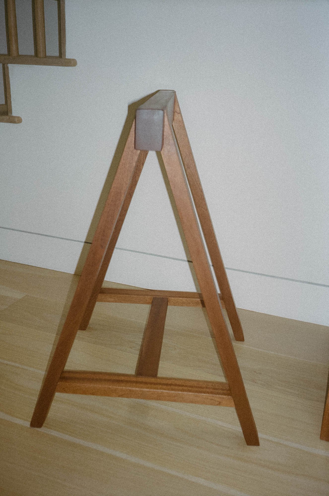 A wooden sawhorse standing on a wood floor against a plain wall.