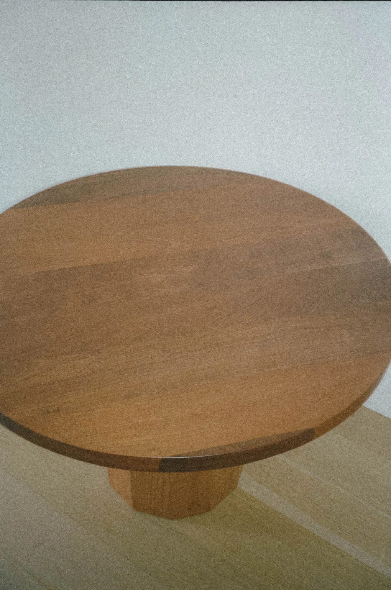 Top-down view of a wooden round table with a central pedestal base, placed on a light-colored, striped wooden floor.