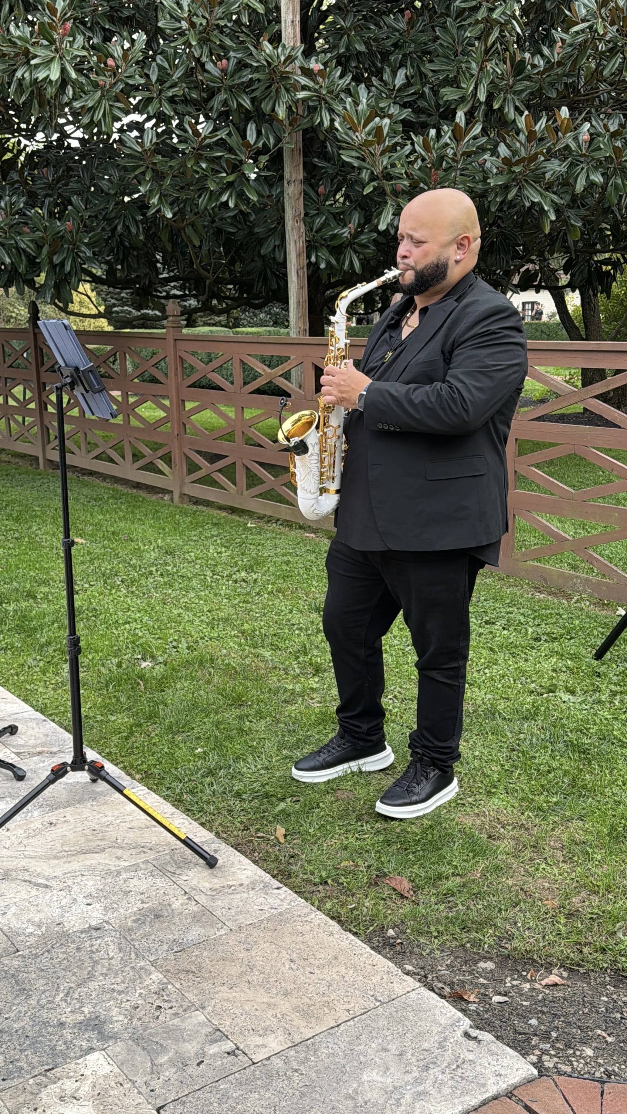 Sax player playing a white and gold sax, dressed in an all black suit