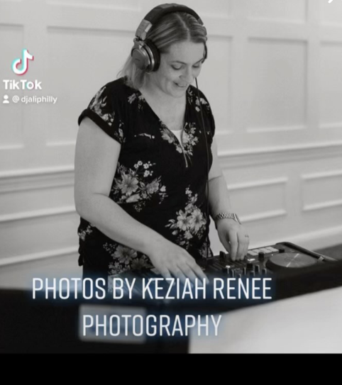 DJ ALi wearing headphones and a floral shirt, DJing with a mixer and turntable in a room with paneled walls, overlaid with text 'Photos by Keziah Renée Photography'.