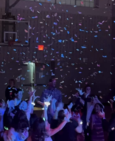 People dancing and celebrating at a party with colorful confetti falling from above.