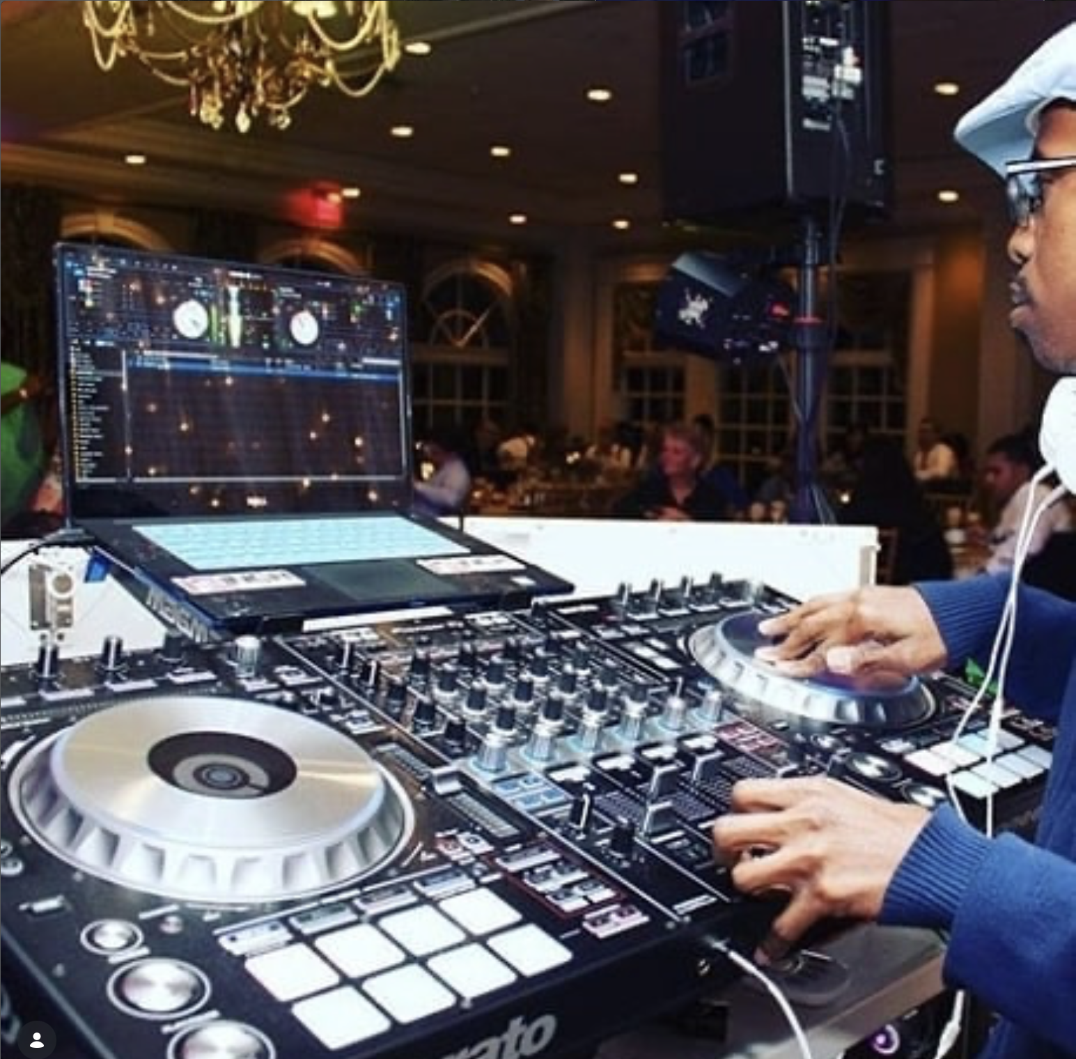 DJ with turntables and mixer at a lively event, people sitting at tables in the background.