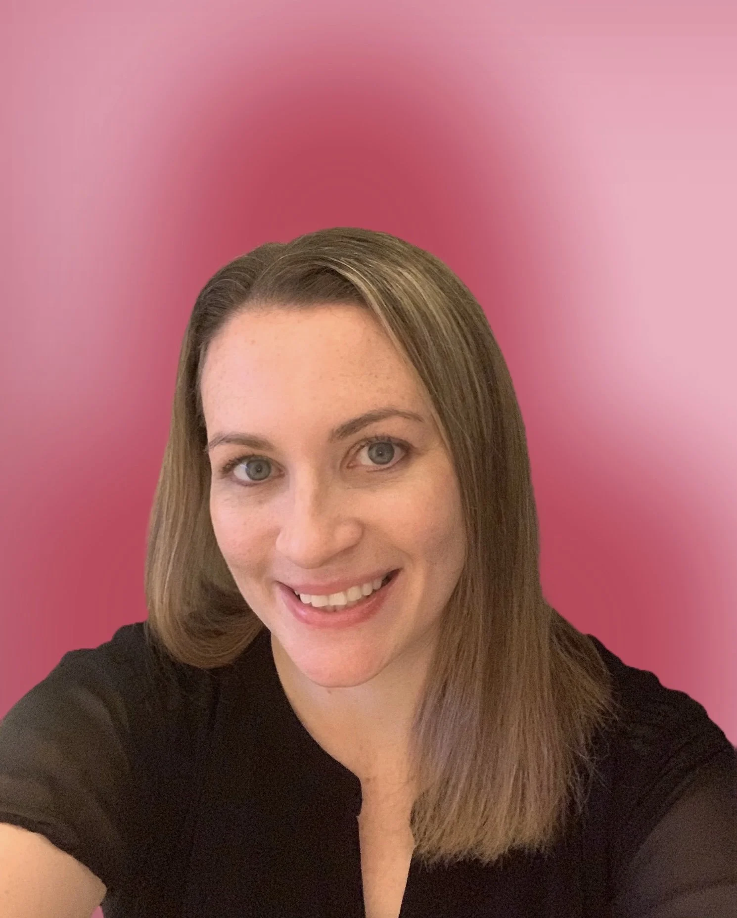DJ Ali with brown hair, blue eyes, smiling, wearing a black top, against a pink background.