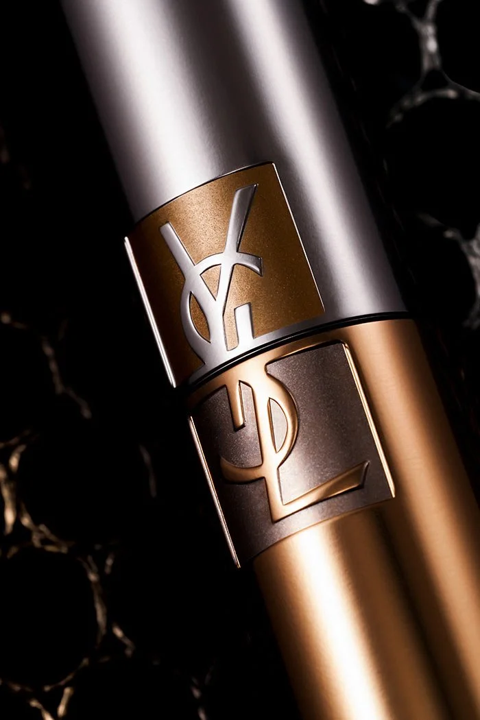 Flacon de parfum de luxe avec logo Yves Saint Laurent en or et noir, posé sur un fond en marbre noir.