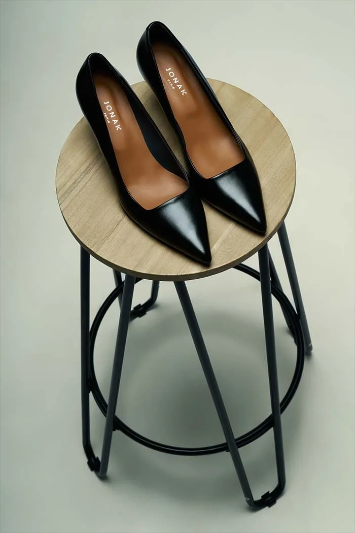 Une paire de chaussures à talons noirs sur une petite table en bois avec un cadre en métal noir.