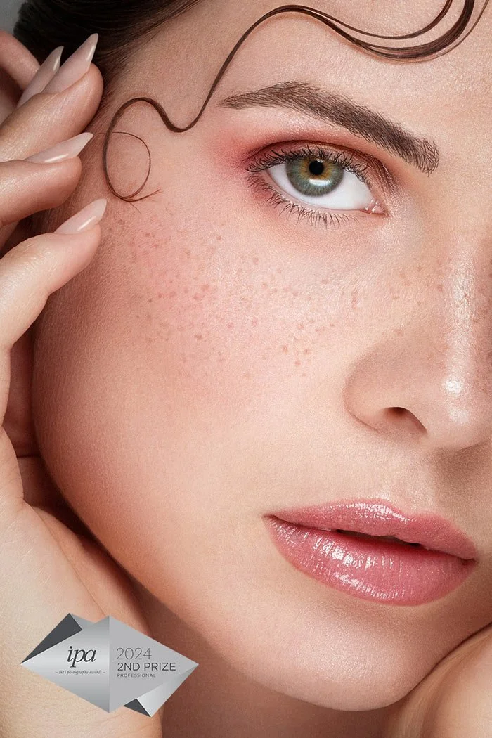 Premier plan du visage d'une femme avec une peau claire, sourcils bien définis, maquillage léger sur les yeux, lèvres légèrement brillantes et cheveux châtains bouclés. Logo du prix IPA 2024, deuxième prix professionnel.