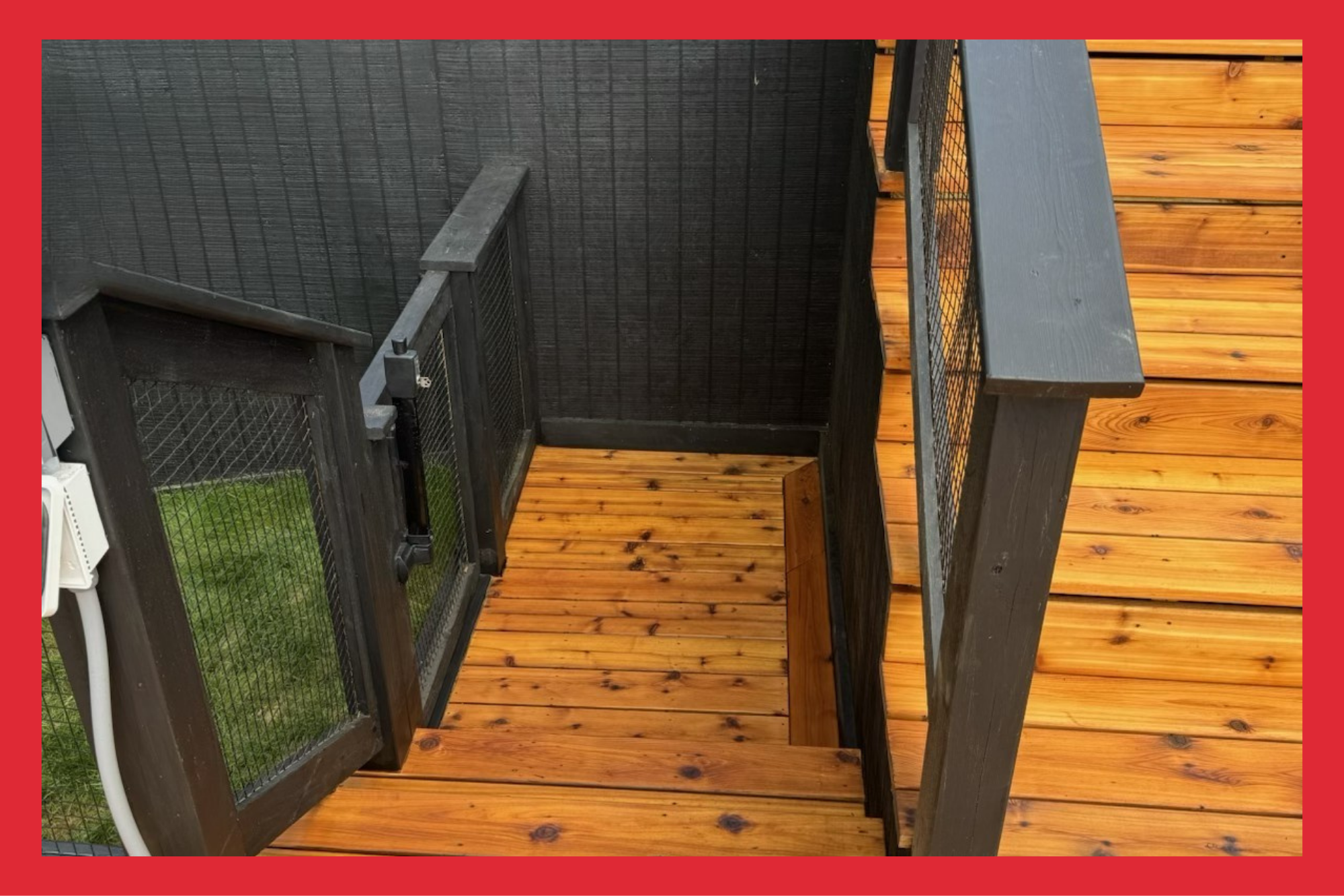 View of a wooden deck with black railing and gate, overlooking a grassy yard, with black and natural wood finish.