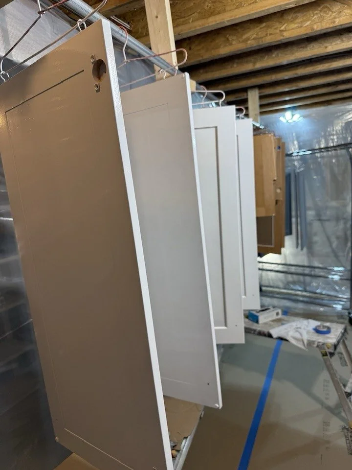 A row of metal cabinet doors hanging in a construction area, with some tools and materials on the floor nearby, and a ceiling with exposed wooden beams.