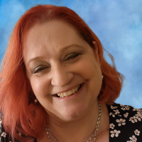 A woman with red hair smiling against a blue sky background.
