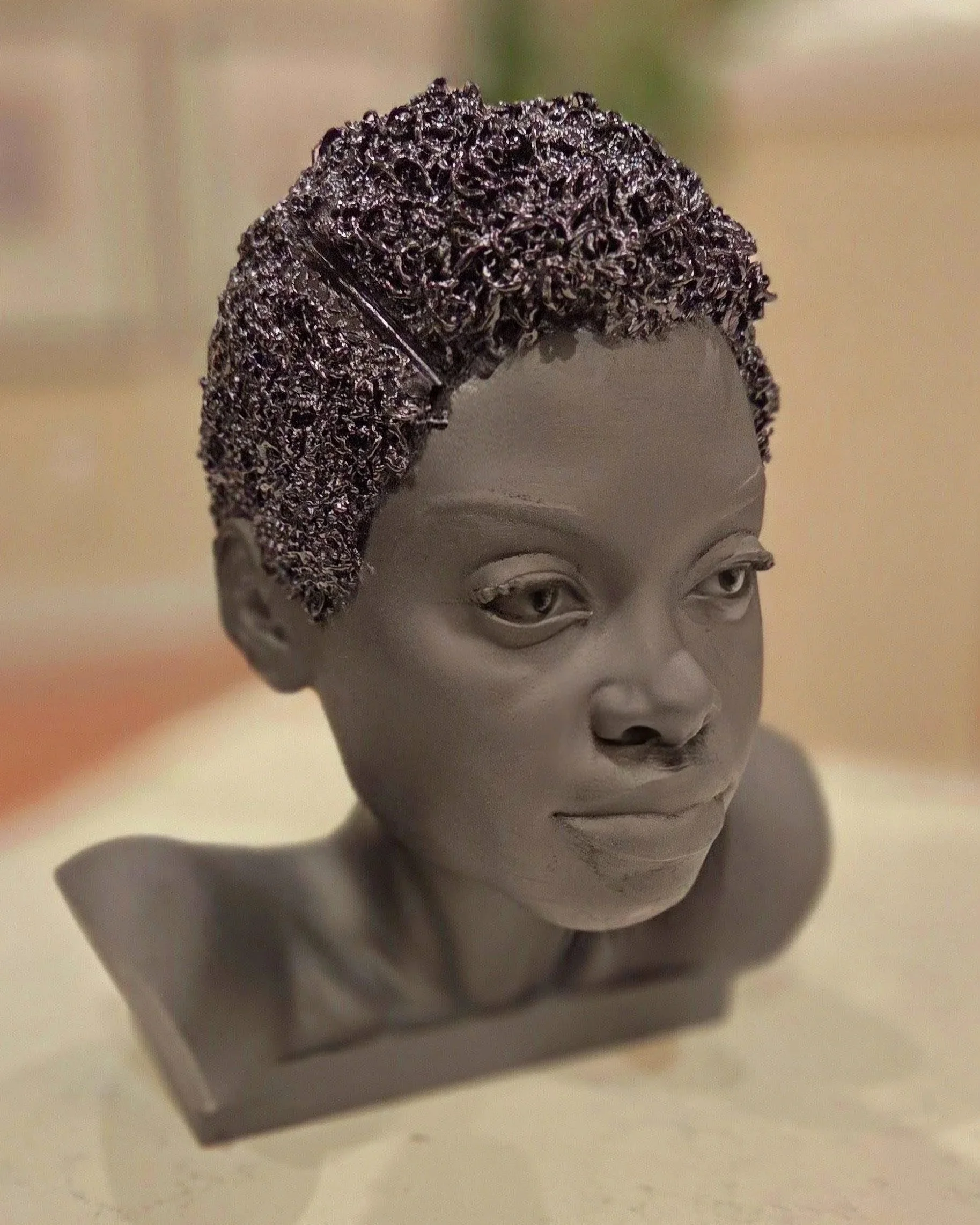 A black sculpted bust of a Nike Onile with curly short hair. The detailed facial is matte black and her textured hair is a shiny black.