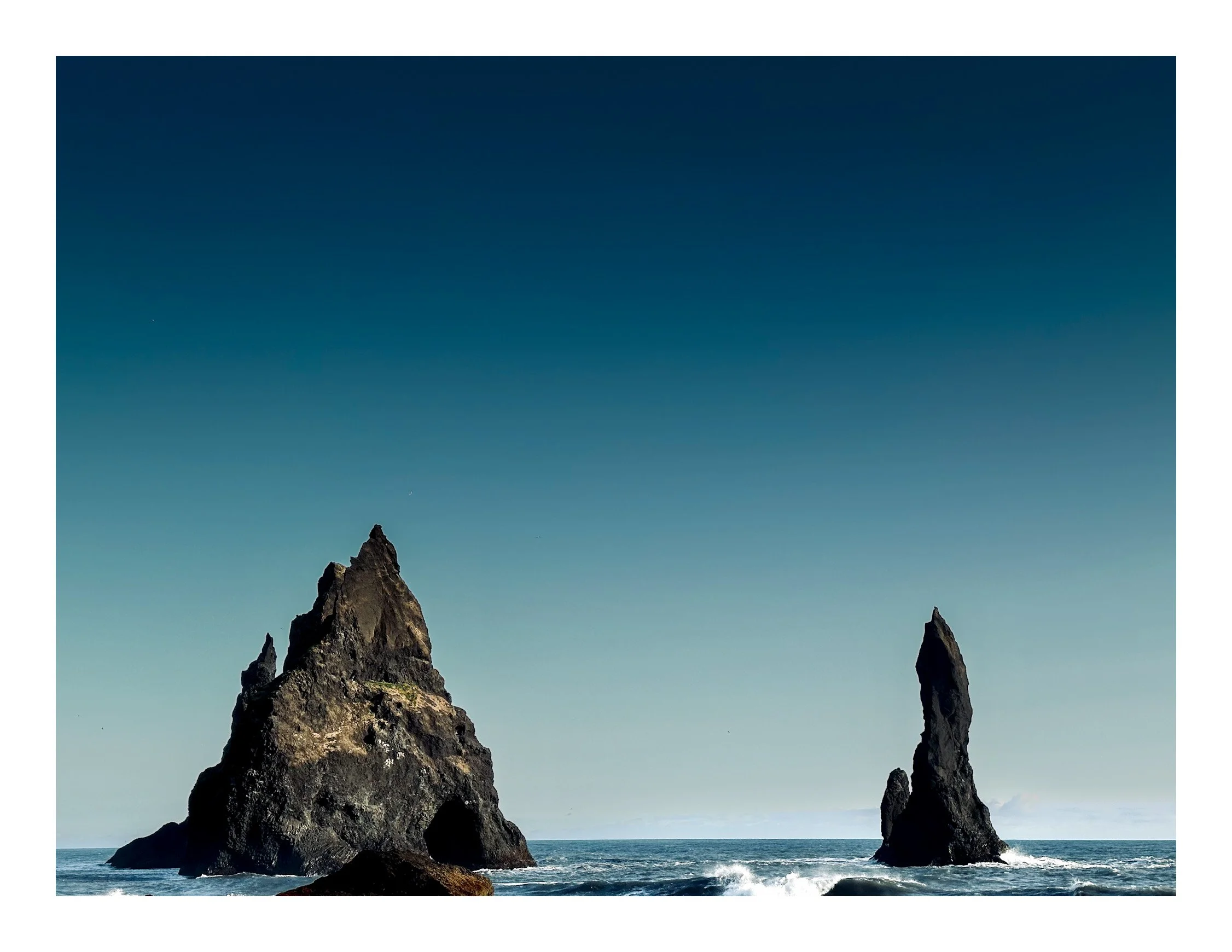 Two tall, jagged rock formations rising from the ocean under a clear sky.
