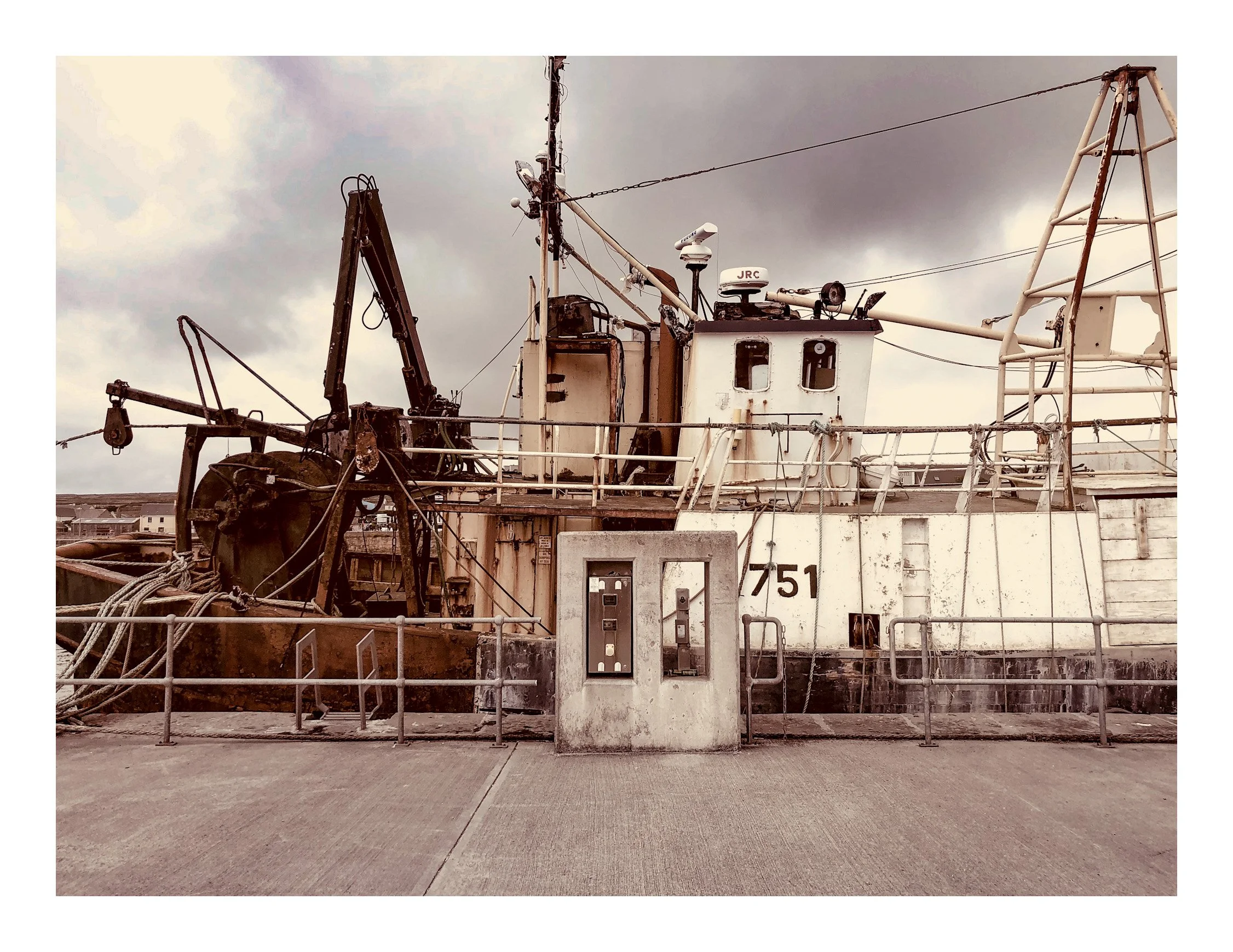 An old, weathered fishing boat with rust and peeling paint, docked at a harbor with overcast skies in the background.