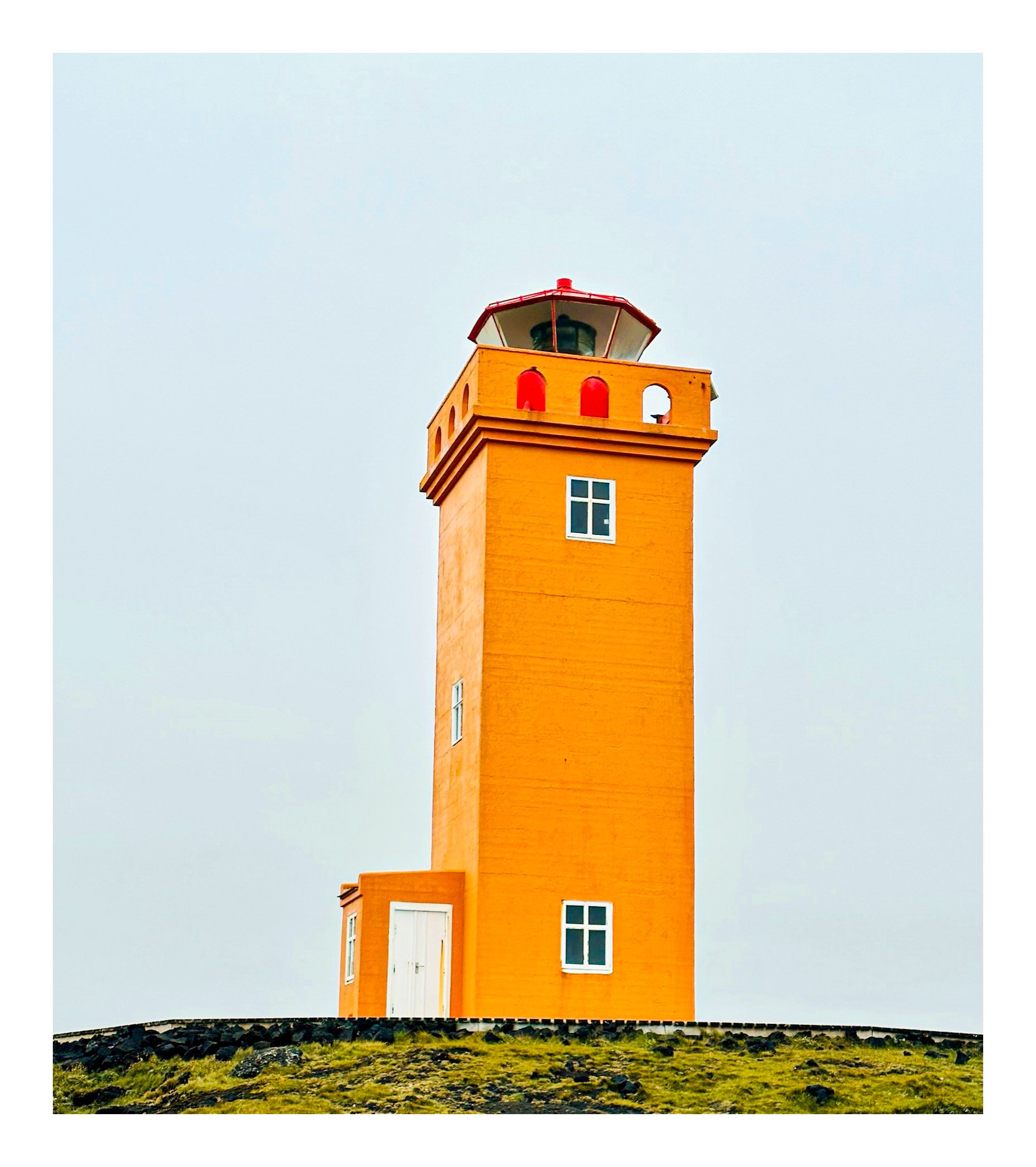 Orange lighthouse on a grassy hill against a cloudy sky.